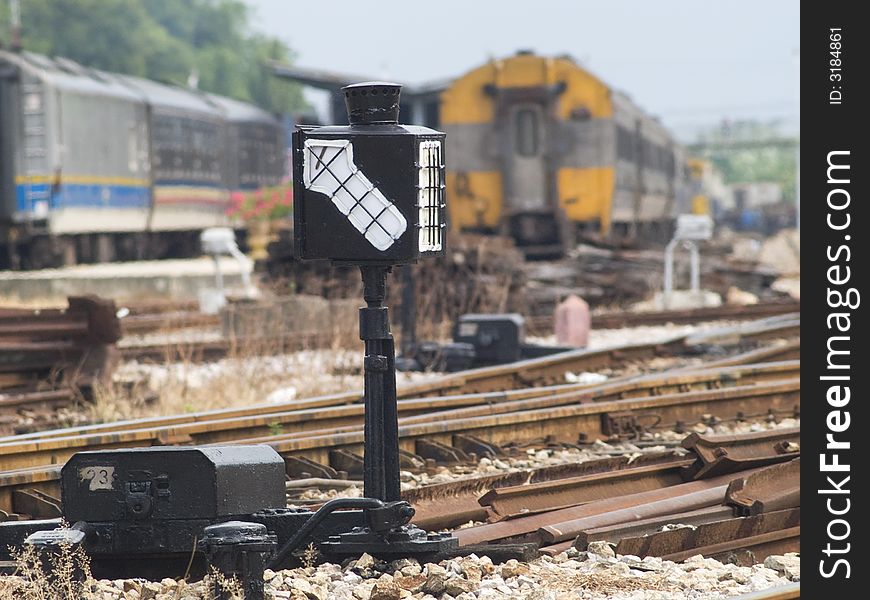 Old-fashioned railway shift signal at a station with trains in the background. Trains blurred out of focus.