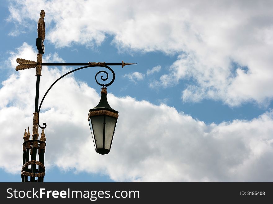 Antique lamp column is photographed against blue sky with white clouds