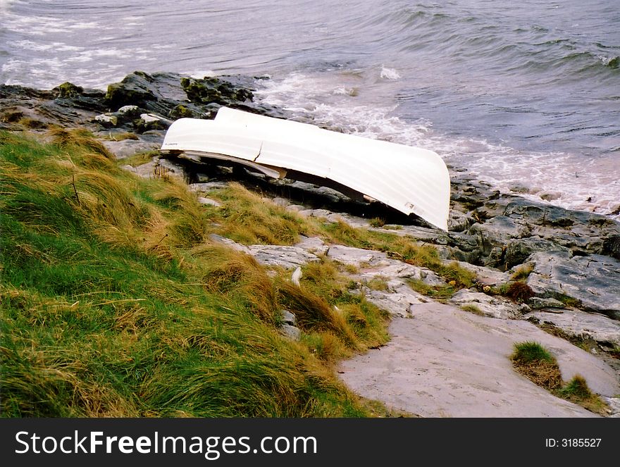 Upturned white boat sitting on rocks by the sea. Upturned white boat sitting on rocks by the sea
