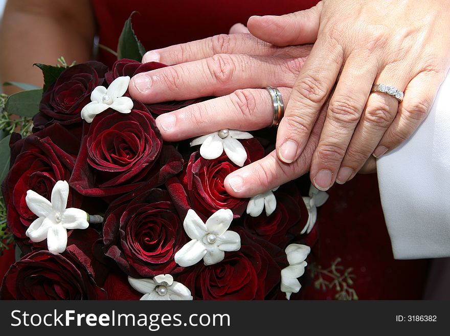 Bride and groom show off their rings over a rose bouquet. Bride and groom show off their rings over a rose bouquet