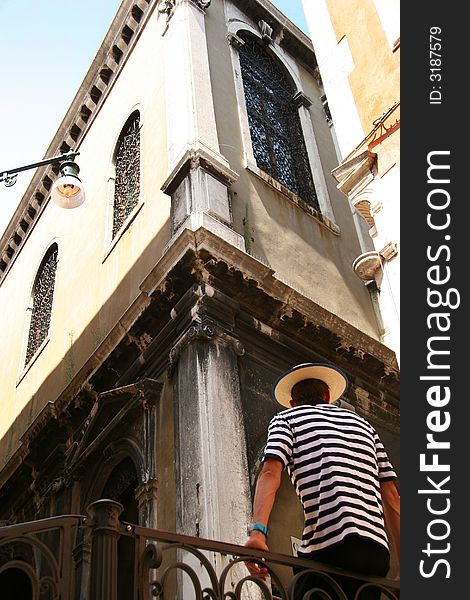 Gondolier sitting on railing with traditional uniform on in venice, italy