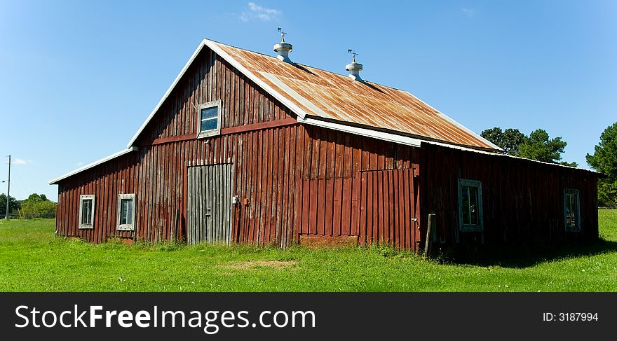 Old red barn against blue sky with green grass in front