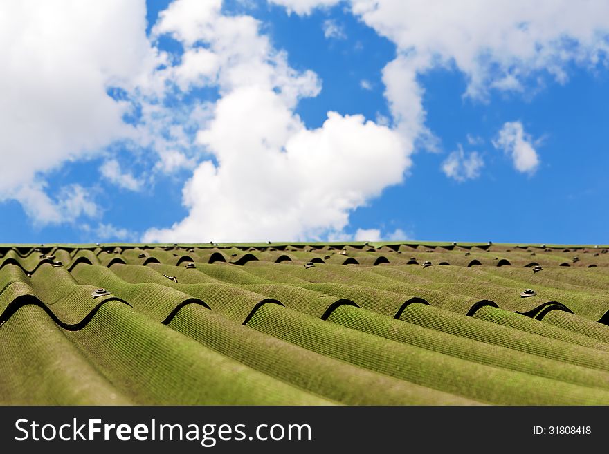 White clouds in blue sky above roof of house