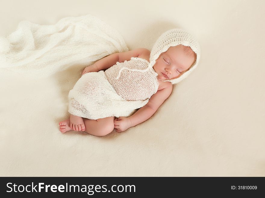 An overhead view of a 13 day old sleeping newborn baby girl. She is wearing a cream colored bonnet and wrapped in gauzy fabric and sleeping on her back. An overhead view of a 13 day old sleeping newborn baby girl. She is wearing a cream colored bonnet and wrapped in gauzy fabric and sleeping on her back.