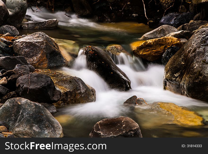 Clear water falling between stones with yellow and orange leaves. Clear water falling between stones with yellow and orange leaves