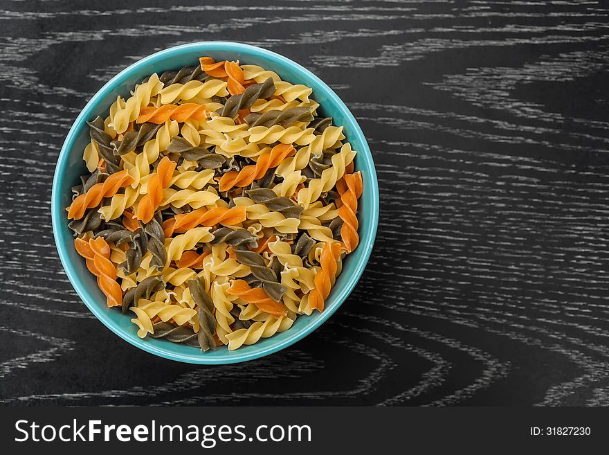 Colorful raw fusilli in blue bowl on black wood table. Colorful raw fusilli in blue bowl on black wood table