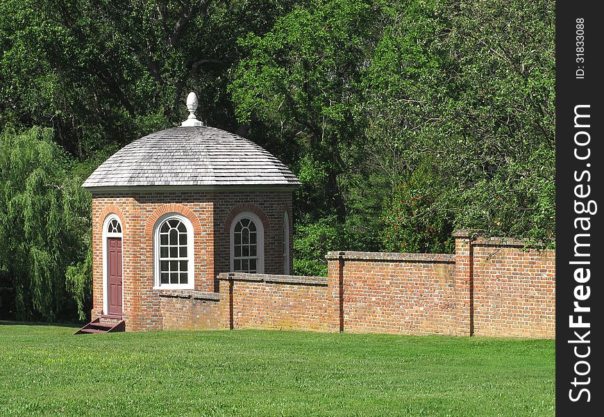 Enclosed brick gazebo attached to a brick wall, with green lawn in front and trees in the background. Enclosed brick gazebo attached to a brick wall, with green lawn in front and trees in the background.