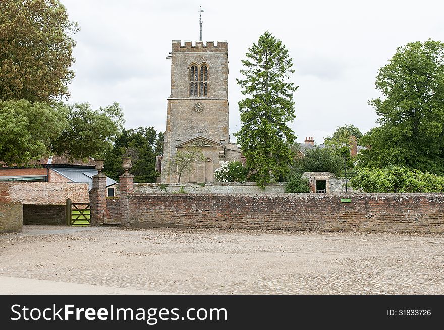 Quaint old medieval church and tower with a cobblestone courtyard and brick wall in the foreground. Chicheley, Buckinghamshire, England. Quaint old medieval church and tower with a cobblestone courtyard and brick wall in the foreground. Chicheley, Buckinghamshire, England