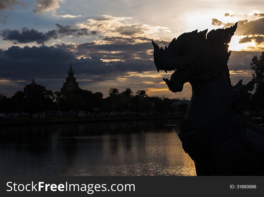 Silhouette lion carved in sunset sky with temple and tree reflection