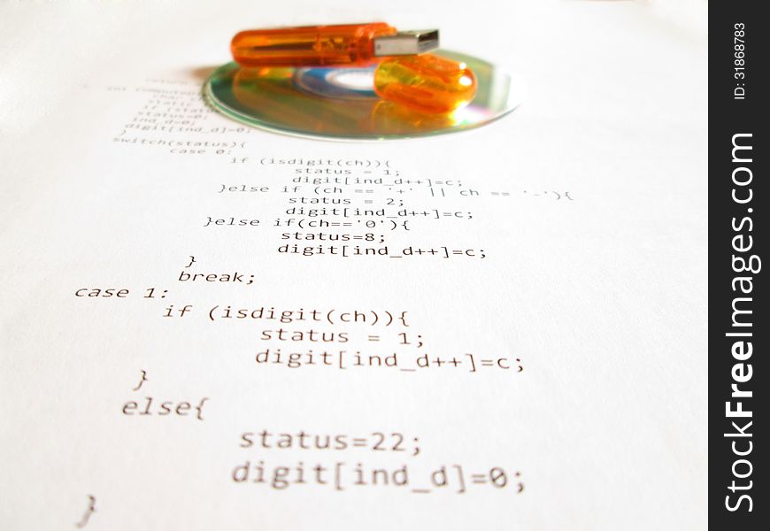 Orange flash drive and mini cd disc over a white sheet of paper with source code. Orange flash drive and mini cd disc over a white sheet of paper with source code.