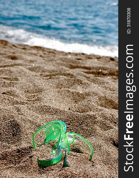 Green flipflop on a beach covered by sand and the sea in the background. Green flipflop on a beach covered by sand and the sea in the background