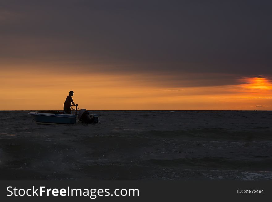 Fisherman anchoring his boat at beach during sunset. Fisherman anchoring his boat at beach during sunset