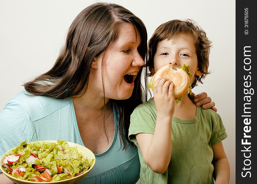 Fat women holding salad and little cute boy with hamburger on white background. Fat women holding salad and little cute boy with hamburger on white background