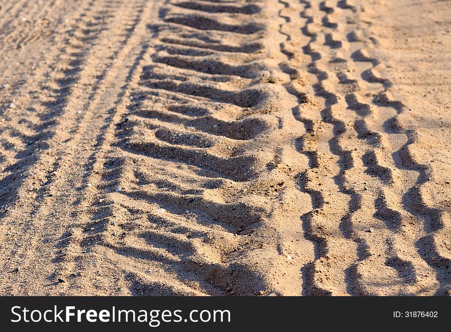 Tire tracks on a sandy road, illuminated by the setting sun