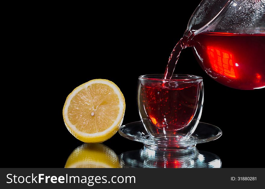 Red tea is poured into a glass cup and lemon close