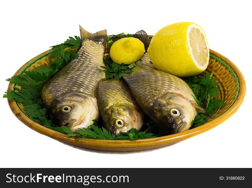 Fresh water fish - carp. Located on ceramic brown the dish with lemon and greens. Fresh water fish - carp. Located on ceramic brown the dish with lemon and greens