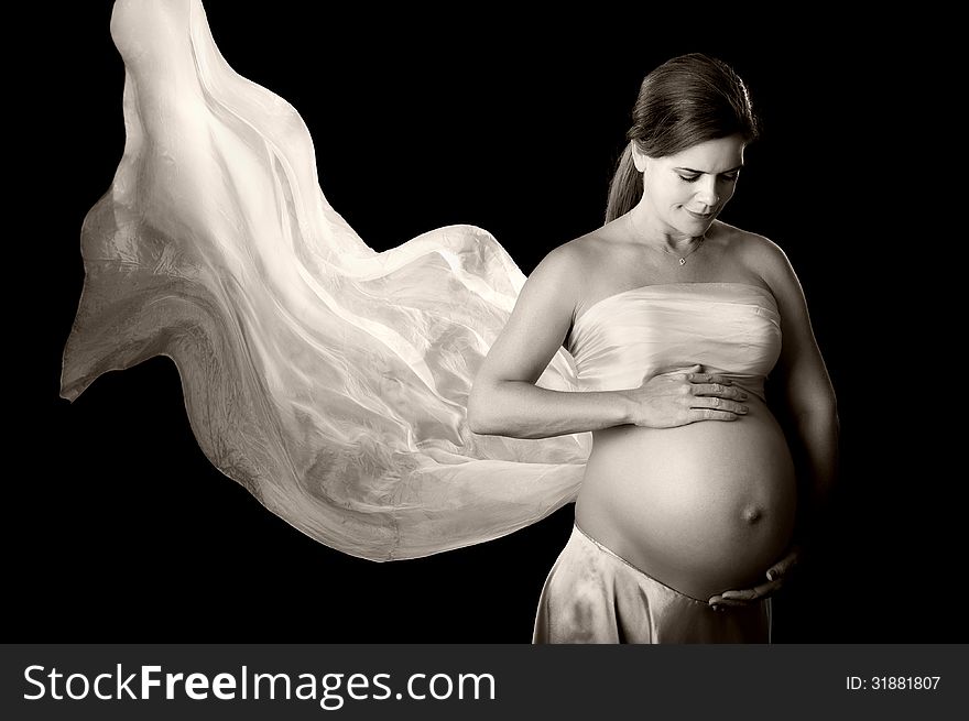 A black and white portrait of a beautiful pregnant woman looking down at her belly and smiling. She has a flowing white silk veil doubling as a bandeau top. A black and white portrait of a beautiful pregnant woman looking down at her belly and smiling. She has a flowing white silk veil doubling as a bandeau top.