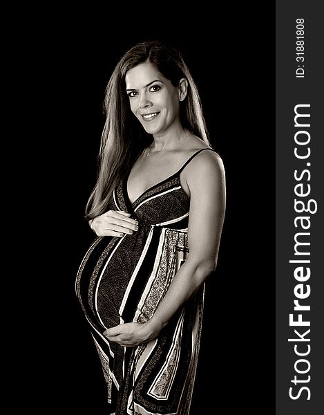 Black and white portrait of a beautiful pregnant woman. She is smiling, looking at the camera and holding her belly. Isolated on a black background.