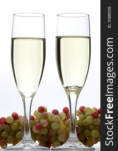 Two glasses of white wine on a white background with grapes. Two glasses of white wine on a white background with grapes