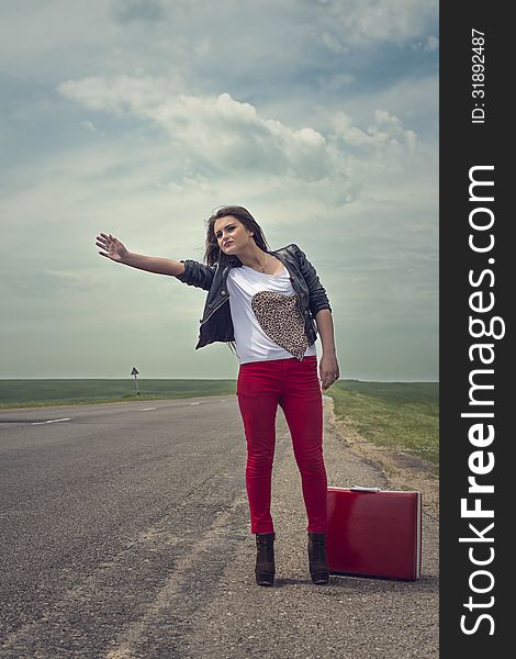 Girl standing on road with suitcase looks for fellow traveler