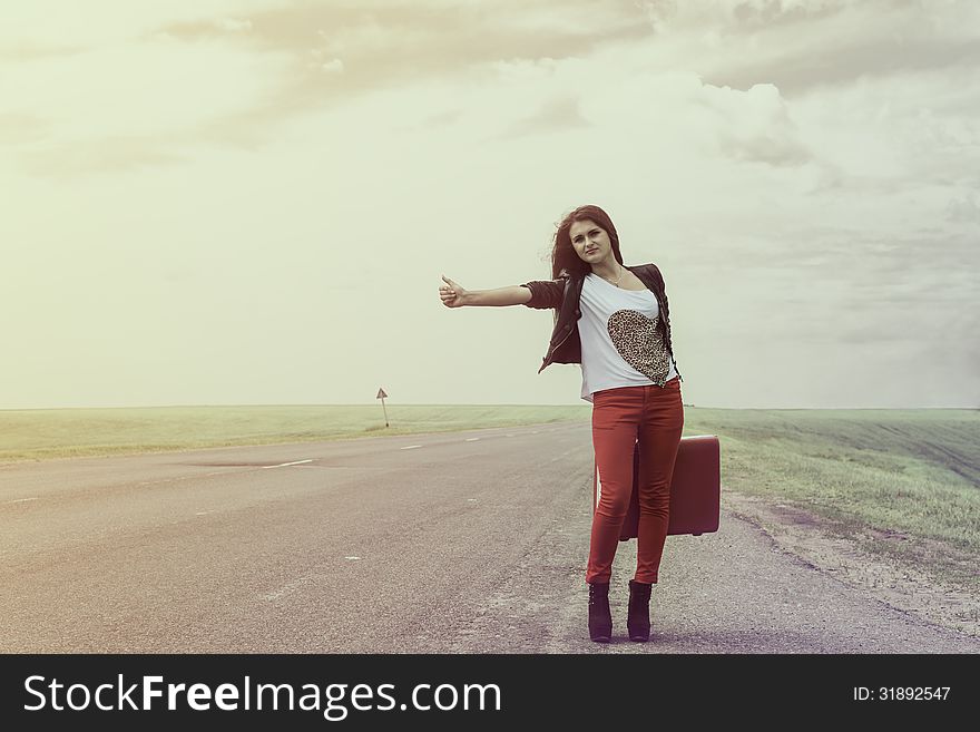 Girl standing on road with suitcase looks for fellow traveler