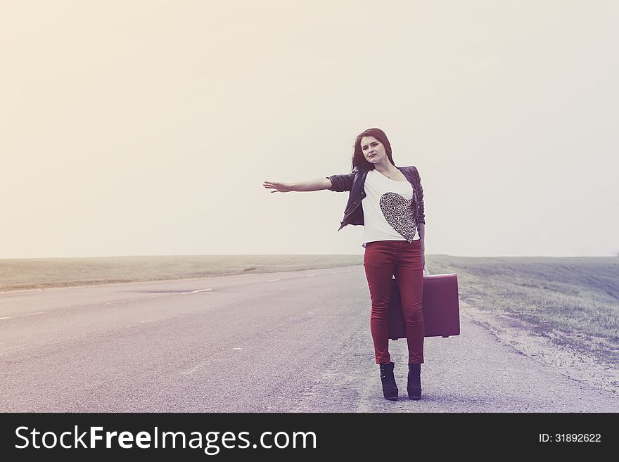 Girl standing on road with suitcase looks for fellow traveler