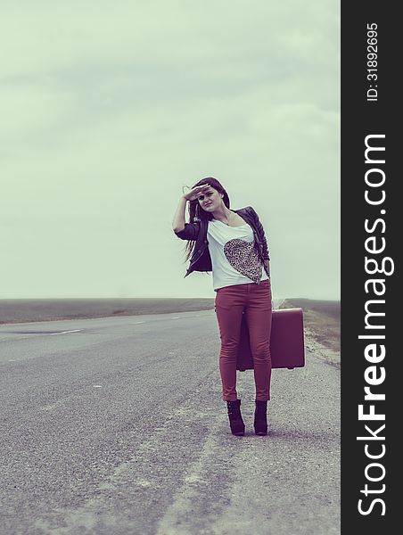 Girl standing on road with suitcase votes and looks for fellow traveler