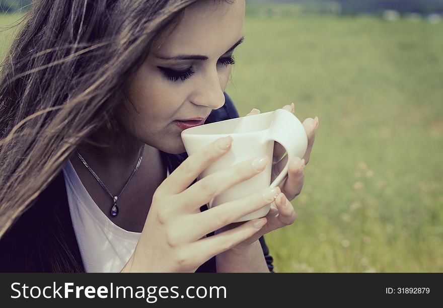 Girl drinks coffee with pleasure out of door