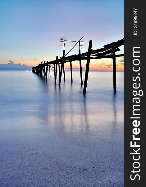 Old wooden bridge in the sea with sunset