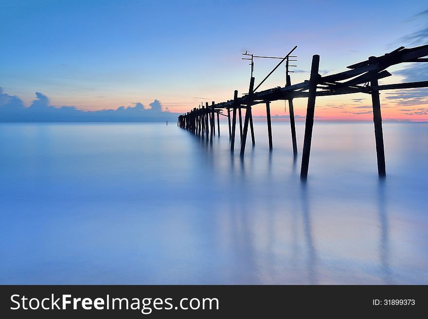 Old wooden bridge in the sea with sunset