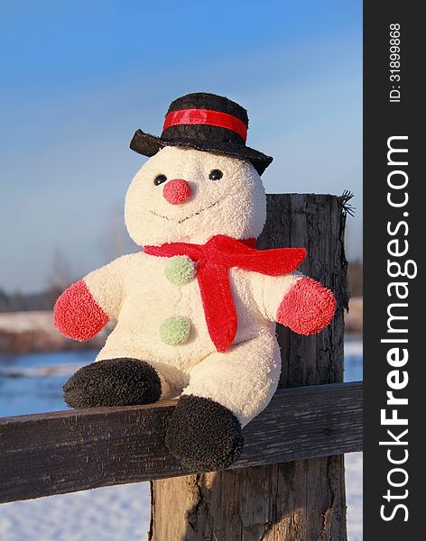 Toy snowman sitting on a wooden fence outdoors in winter. Toy snowman sitting on a wooden fence outdoors in winter