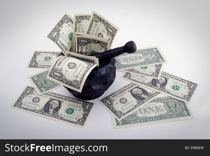 Grinding for Dollars - Wood mortar and pestle containing dollar bills on a white background.