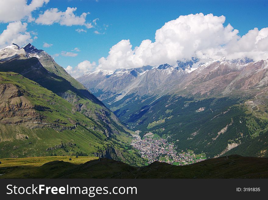 A panoramic view on Swiss Alps rocky mountains with village in valley under cloudy sky, horizontal. Zermat, Switzerland, Europe. A panoramic view on Swiss Alps rocky mountains with village in valley under cloudy sky, horizontal. Zermat, Switzerland, Europe.