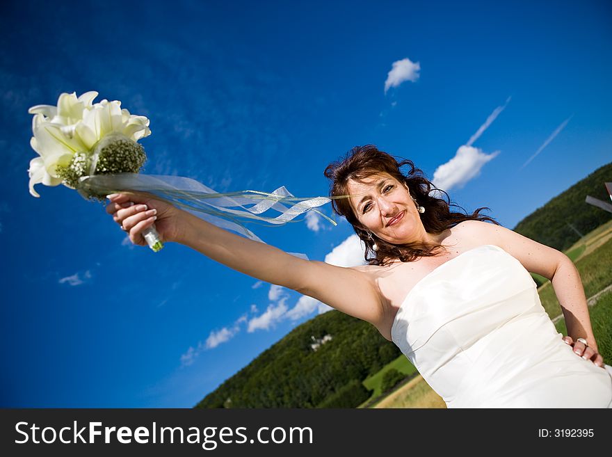 Fancy Perspective. Bride holds her bridal bouquet on outstretched arm. Deep blue sky as background. Sunny weather. Adult bride. Fancy Perspective. Bride holds her bridal bouquet on outstretched arm. Deep blue sky as background. Sunny weather. Adult bride.