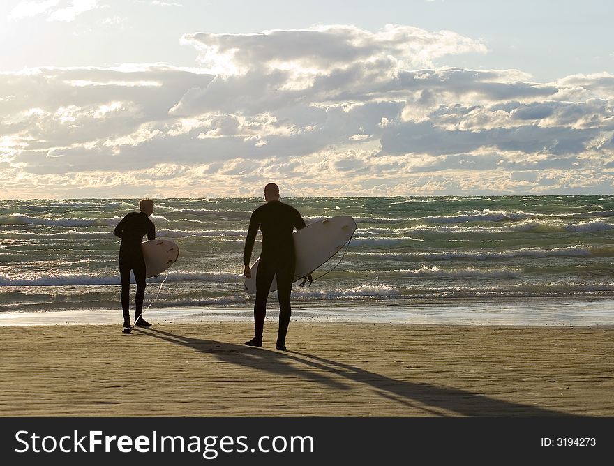 Men casting long shadows on the beach and preparing to surf the waves at sunset. Men casting long shadows on the beach and preparing to surf the waves at sunset