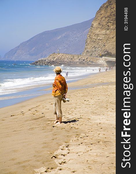 A retired matured woman is watching other beach goers. A retired matured woman is watching other beach goers