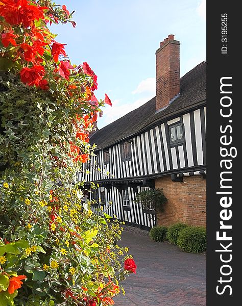 Half timbered Tudor cottages framed by a large display of flowers and shrubs. Focus on the cottages.