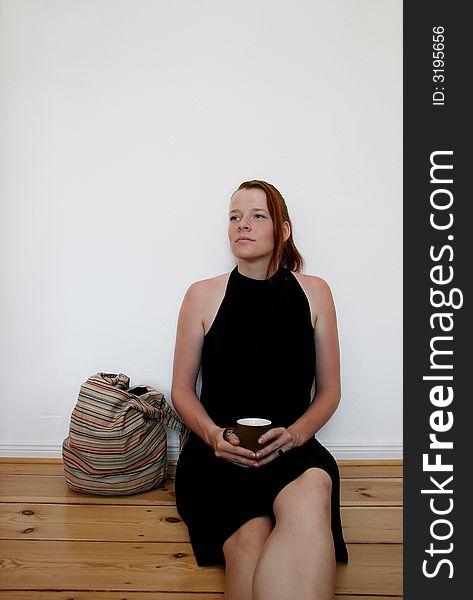 A young woman, possibly a student, relaxing during her coffee break with a cup in her hands, leaning against a white wall. A young woman, possibly a student, relaxing during her coffee break with a cup in her hands, leaning against a white wall.