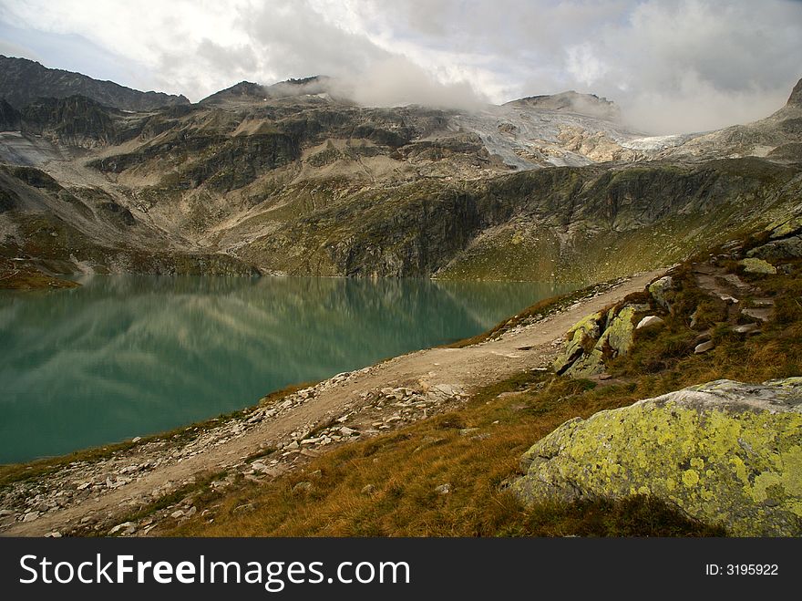 Alpine lake (WeiÃŸsee) surrounded by mountains with low clouds.