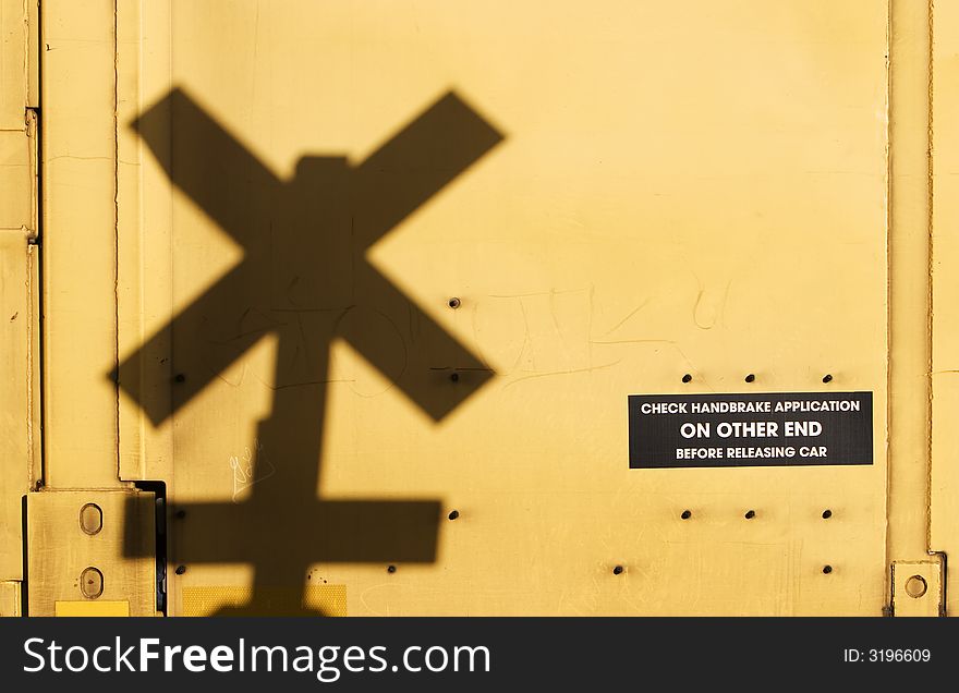 Shadow of a railroad crossing sign cast against the yellow side of a freight train car. Shadow of a railroad crossing sign cast against the yellow side of a freight train car.