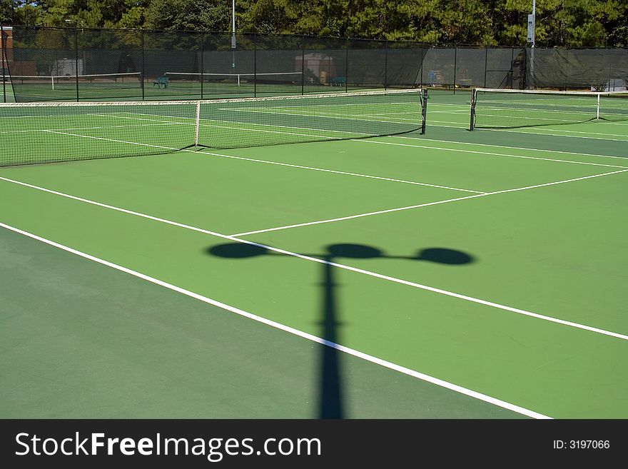View of an empty tennis court with a shadow from a light. View of an empty tennis court with a shadow from a light