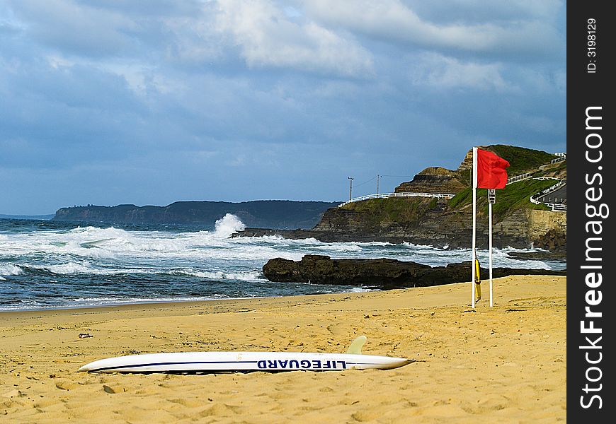 An empty beach with the lifeguard rescue board on the sand and red closed flag. An empty beach with the lifeguard rescue board on the sand and red closed flag