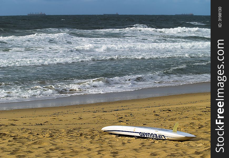 A lifeguard rescue board on the beach with ships on the distant horizon