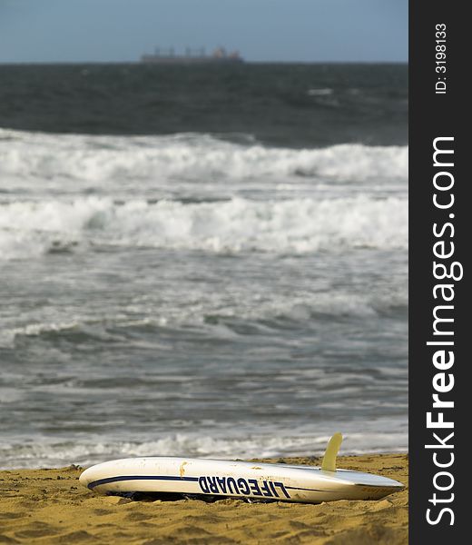 A lifeguard rescue board on the beach with a ship on the horizon
