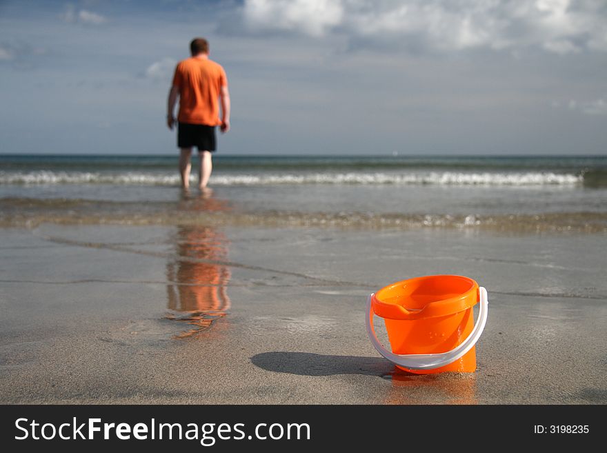 Brigh orange sand bucket with water on the beach and boy on the background. Brigh orange sand bucket with water on the beach and boy on the background