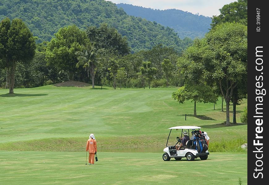 Caddie and golf cart on the fairway of a par 5 hole in tropical setting