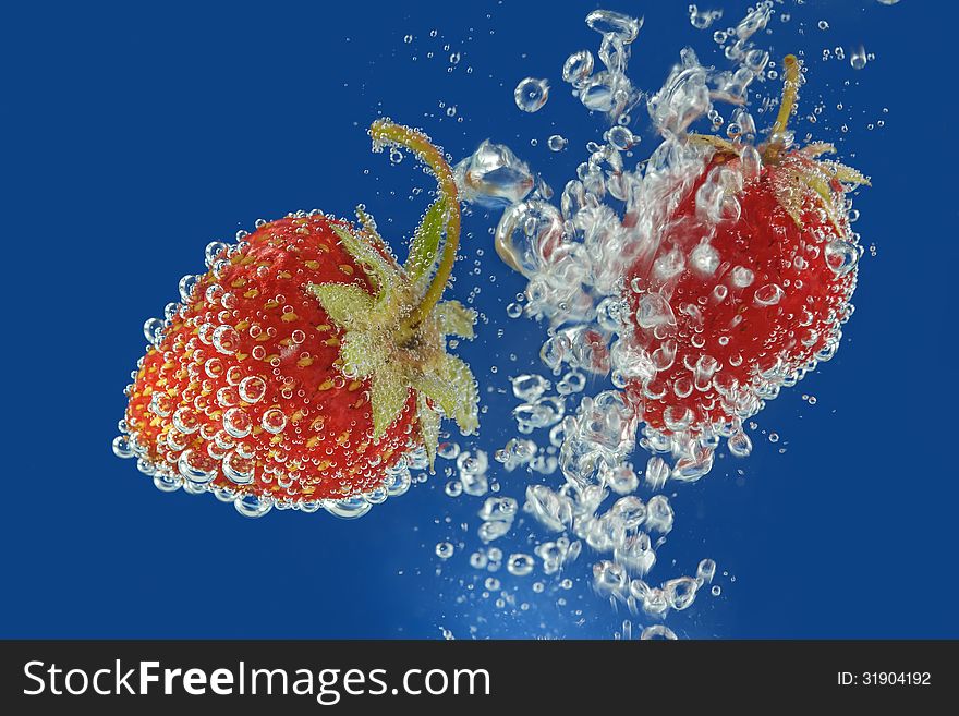 Splashes of water surrounding a fresh strawberry on a blue background