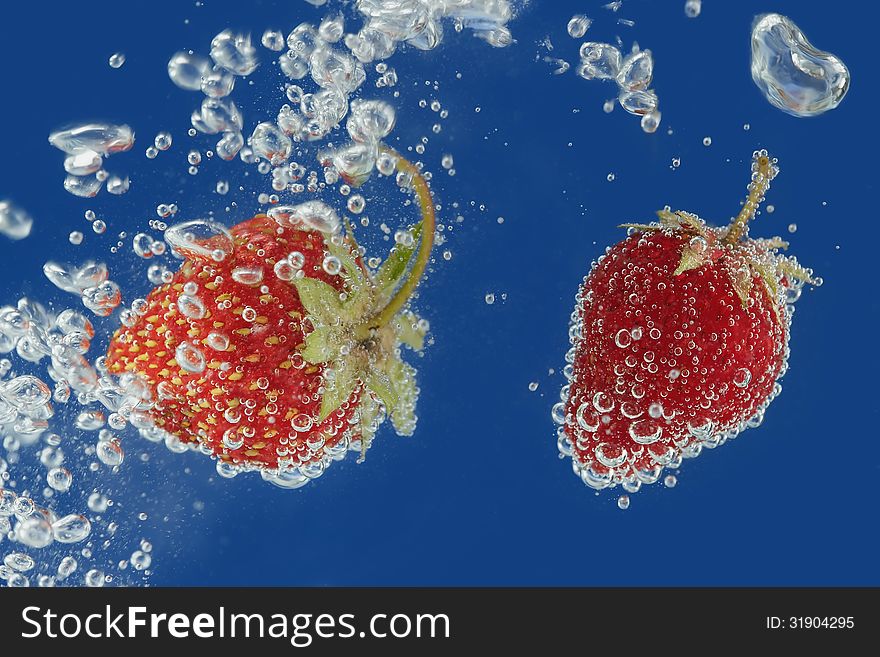 Splashes of water surrounding a fresh strawberry on a blue background