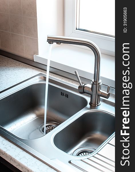 A stainless steel kitchen faucet includes a sink, water flows from the tap.