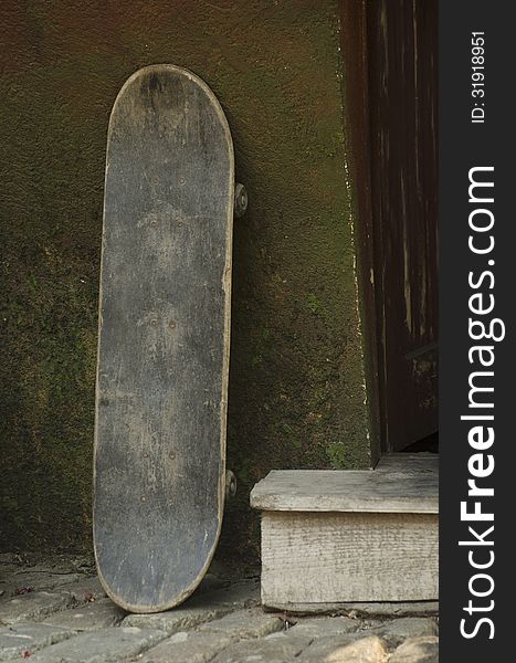 An old and used skateboard near an entrance door. An old and used skateboard near an entrance door